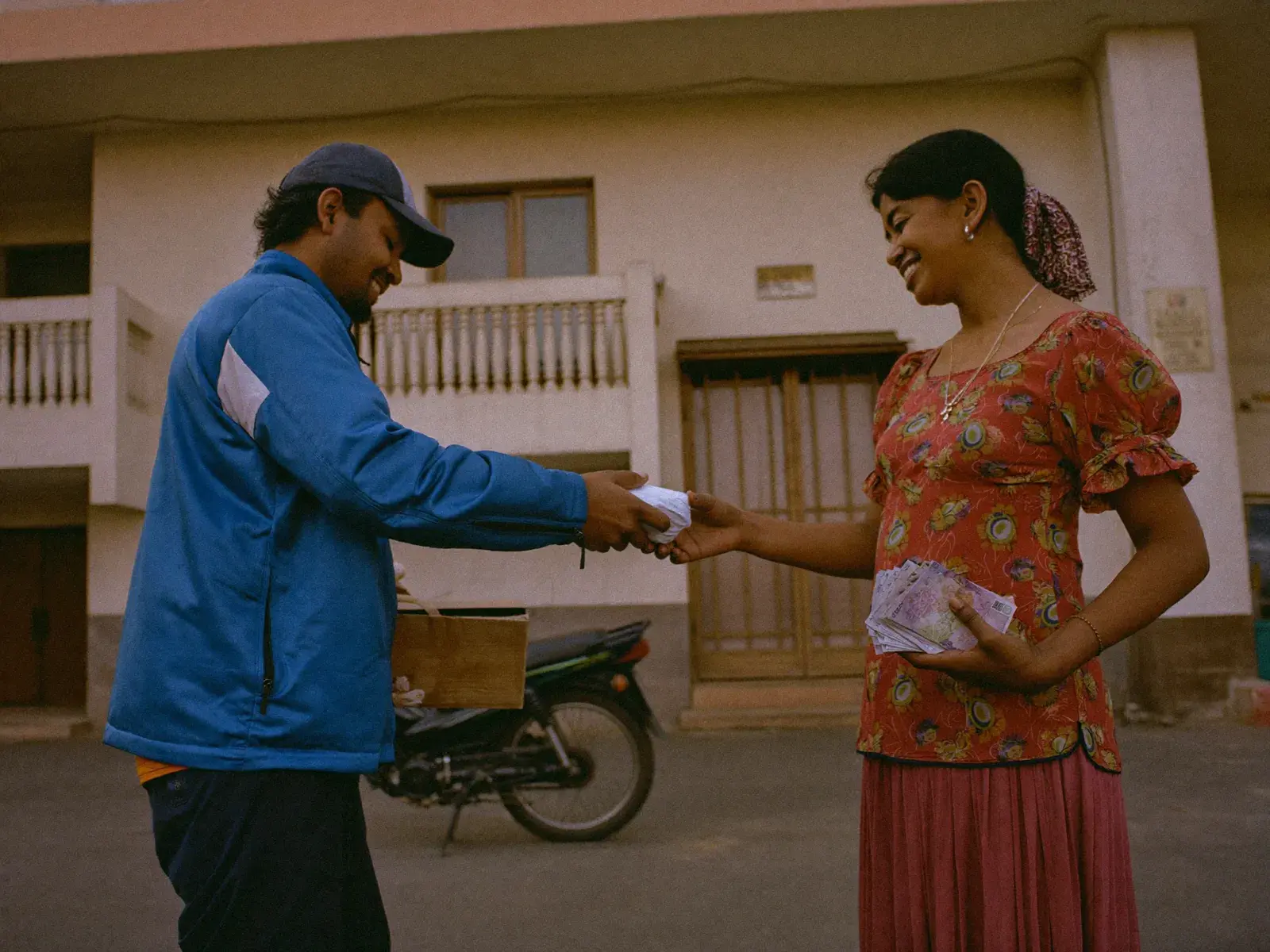 Delivery rider handing a parcel to a customer who pays cash at her building gate