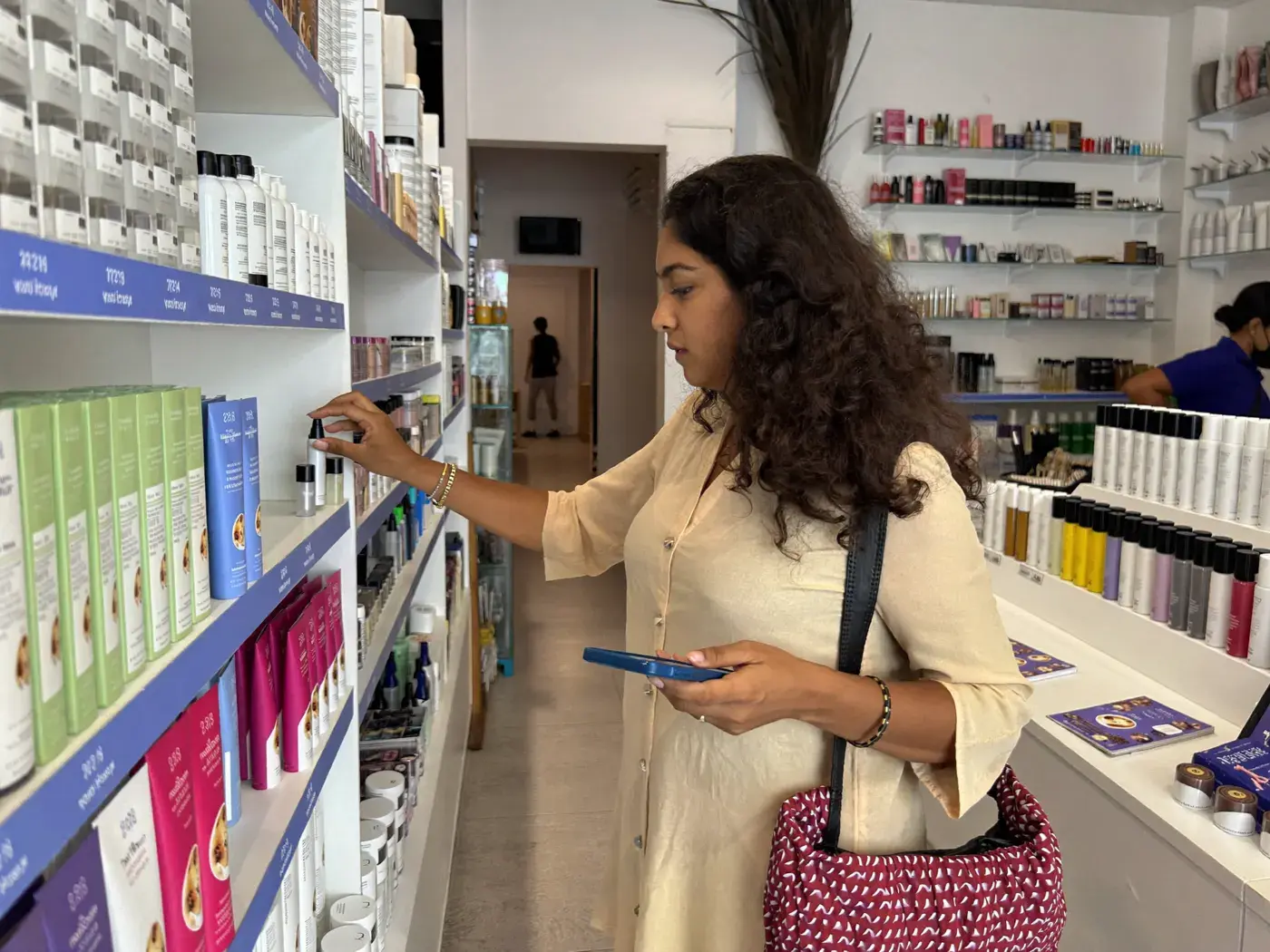 Shop owner checking an order on a phone beside a shelf of skincare products